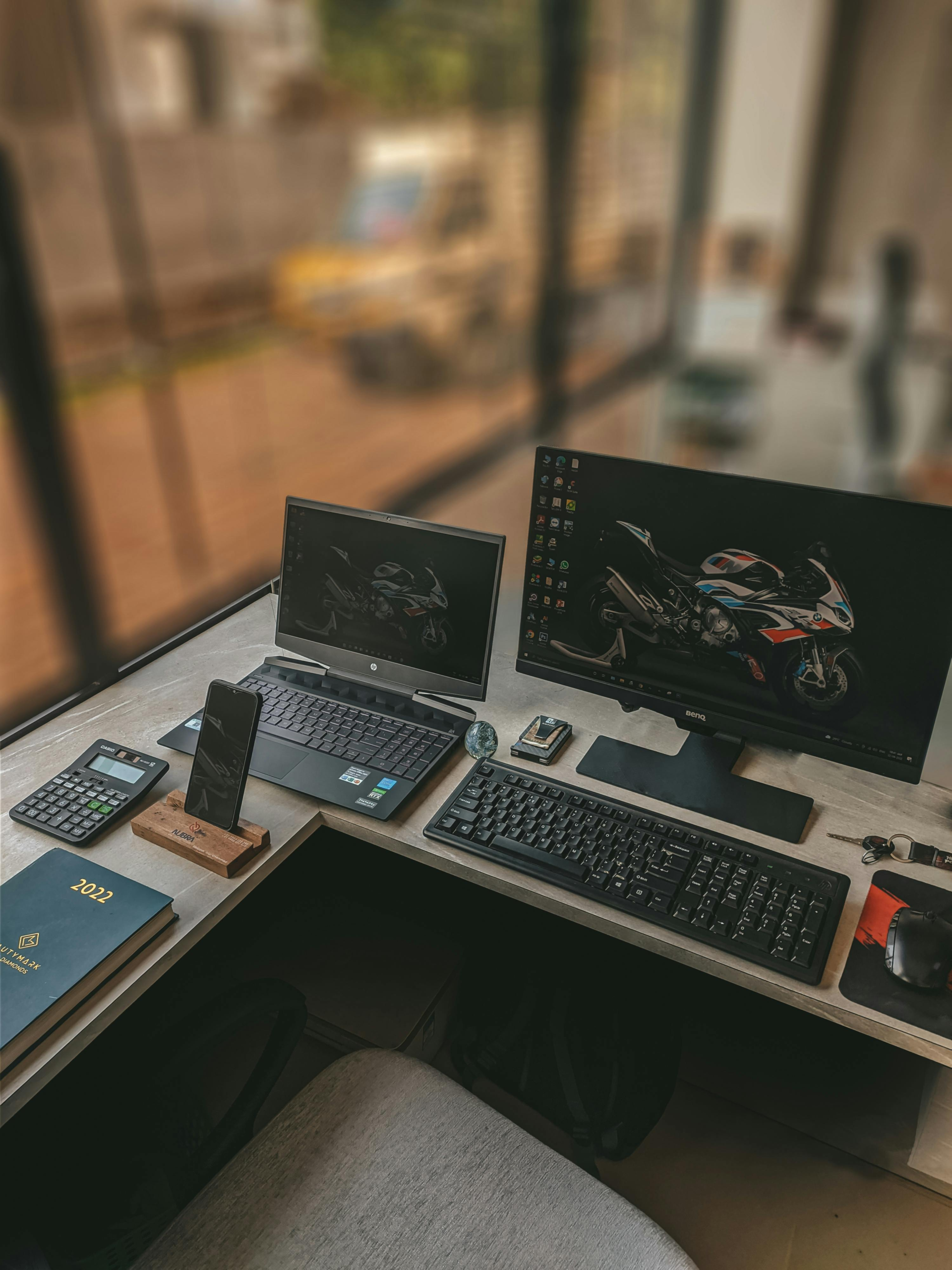 A modern workspace featuring dual monitors, laptop, phone, and office supplies.